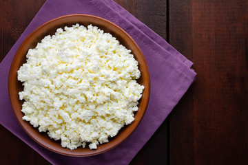 Cottage cheese on wooden boards. Fresh cottage cheese in a ceramic bowl. Clay plate with soft cheese on a linen napkin. Top view. Copy space