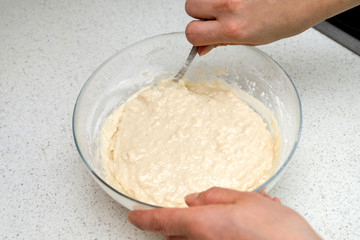Woman's hands with an yeast dough. The woman is stirring the baking dough in a glass bowl.