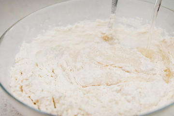 Preparation of the yeast dough. Adding water to the dough in the glass bowl.