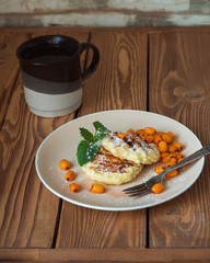 Serving of two cottage cheese pancakes with sea buckthorn ice cream on a ceramic brown plate and brown coffee beans