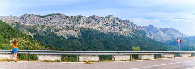 Asphalt road and sign in the mountains. Panorama view of the mountains on the left. Girl looks at...