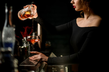 Professional woman bartender masterfully pours drink into glass