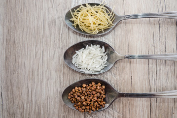 composition with various types of legumes and cereals in spoons on a wooden table. Organic grains. Macrons, rice and buckwheat. View from above.