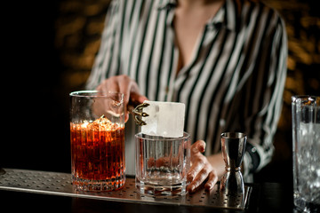 close-up. Female bartender holding large ice cube over glass