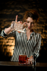 Beauty woman bartender gently pours alcoholic drink from mixing cup into large glass with ice