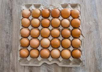Chicken eggs in a cardboard box on a wooden table.