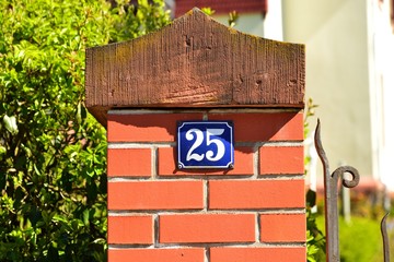 Hausnummer 25 aus emailliertem Blech an einem roten Backsteinpfeiler einer Grundstücksmauer