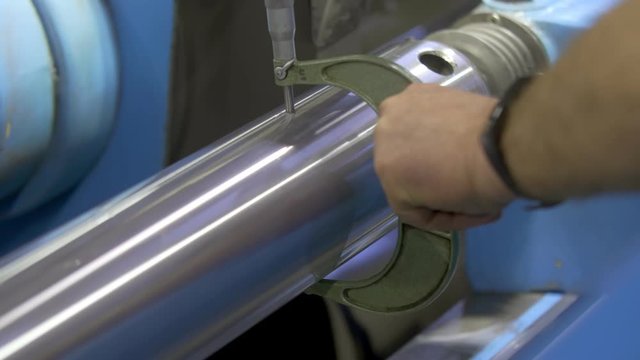 Male hands of the worker measure the size of the steel shaft with a micrometer after processing on the grinding machine. CNC metal grinding machine.