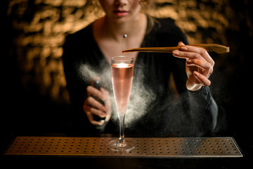 Close-up. Young girl bartender carefully decorates glass of rose drink and sprinkles on it