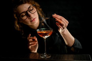 Close-up. Young female barman adding ingredient to glass with drink