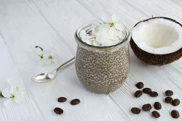 Coffee pudding with chia and coconut flakes  in the glass jar on the white  wooden background. Closeup.