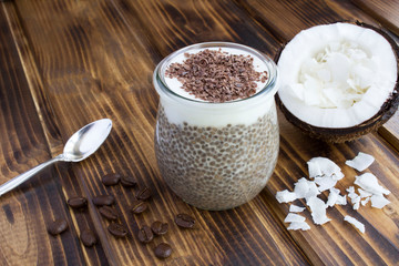 Coffee pudding with chia, coconut flakes  and chocolate in the glass jar on the brown  wooden background. Closeup.