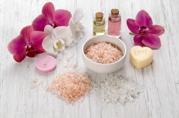 Fototapeta na wymiar Bath salts, pink Orchid flower, candle and soap on white wooden background as Spa concept body care at home or salon