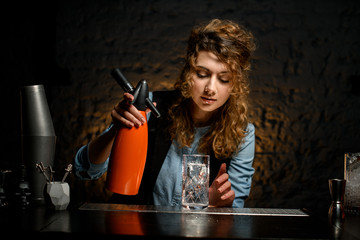 girl at bar holds siphon in her hand.