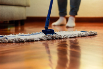 A woman cleaning the hardwood floor, with a close-up of the mop and a blurred background of feet...