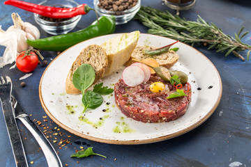 Steak Tartare with bread toasts and egg on top on blue background