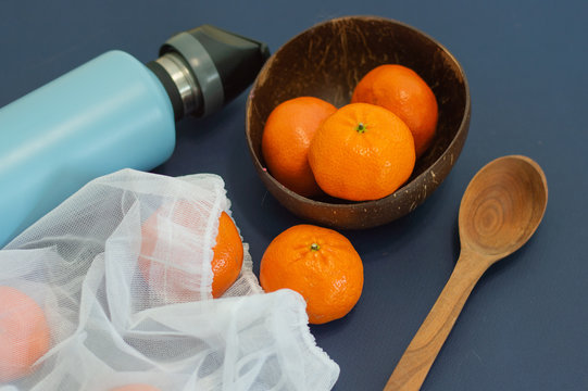 Blue eco steel bootle with eco zero-waste reuse baf with fruits -  mandarines, with are on coconut plate on blue background.