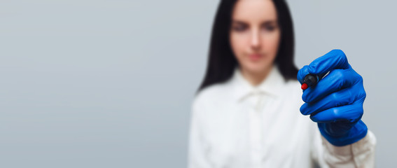 A female hand in a medical glove and in a white smock holds a pen and writes in the air on a gray...
