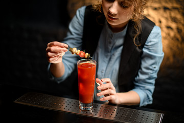 Lady at bar gently decorates glass with Bloody Mary cocktail
