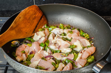 Cooking sliced onions, green peppers and chicken breasts on a frying pan close up.