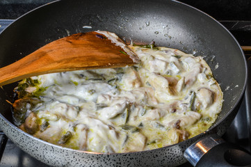 Simmering sliced onions, green peppers and chicken breasts with cooking cream on a frying pan close up.