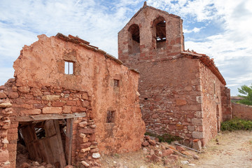 Ruins of a house of red stone, near a church in an abandoned village 