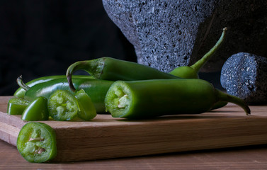 Molcajete and serrano peppers or chiles serranos on a wooden cutting board chiaroscuro, low key...