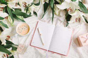 Opened notebook, coffee cup and flowers on the white bed sheet. Good morning and weekend concept in flat lay style