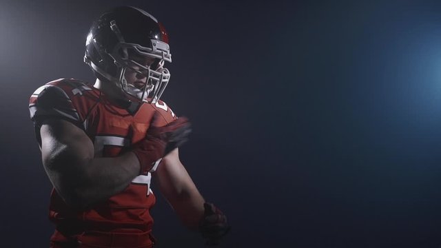 Portrait of determined professional American football player in helmet in dramatic light stretching before the game. Confident spotsman in uniform. Usa team game and extreme sport spirit concept.