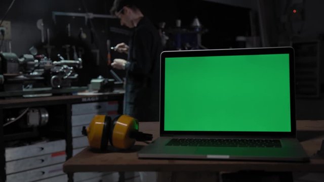Laptop with a green screen on the background of the industrial environment. A worker works for a milling machine. The concept of production and construction