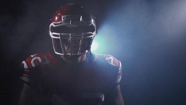 Portrait of determined professional American football player in helmet in dramatic light ready for game. Masculine and agression. Confident man in uniform. Usa team game, extreme sport spirit concept.