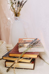 a stack of books on the table, and in the background a vase of flowers