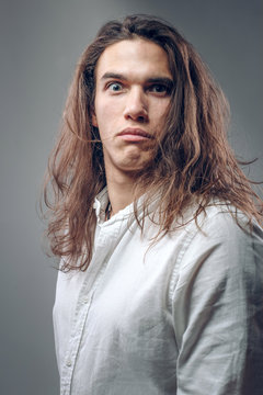 Funny guy with surprised expression. Comic cheerful young man with long hair on isolated background in studio