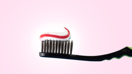 Multi-colored toothpaste on a black toothbrush. Toothbrush on a pink background.