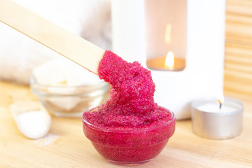Natural pink body scrub made from sugar. Pink scrub in a glass cup on a background of candles and sugar.
