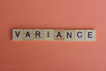 text from a brown word variance made of small wooden letters with black font on a pink table