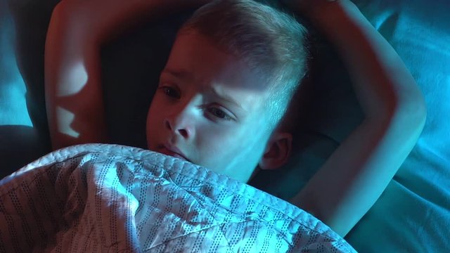 portrait boy in bed with his eyes open. the child is afraid of ghosts. tormented by nightmares and terrible dreams in children