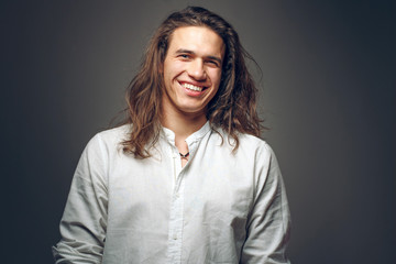 Handsome happy man in white shirt. Smiling guy with long hair on isolated background in studio....