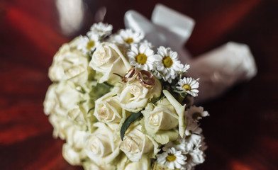 Wedding bouquet of white roses with golden rings close-up.