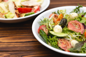 white deep plates with fresh salad ingredients mixed with sauce placed on a rustic background. A place for a menu, banner or advertisement