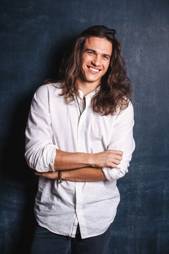 Handsome happy man in white shirt. Smiling guy with long hair on isolated background in studio. Sexy confident boy