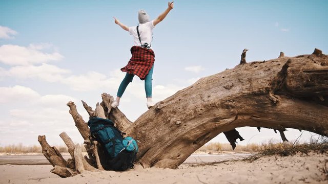 Happy young woman standing on the tree trunk on the sandy beach with outstretched hands. Backpacker enjoying freedom.