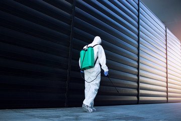 Shot of exterminator person in white chemical protection suit doing disinfection and pest control and spraying poison to kill insects and rodents. Successful pest control and extermination.