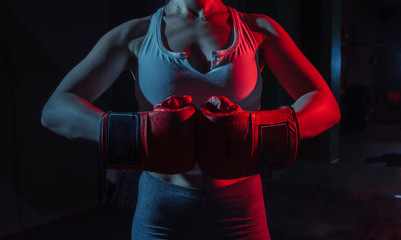 Female boxer with boxing gloves on her hands in neon blue red light on a dark background.