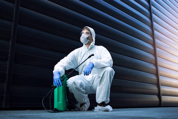 Pest control. Man in white protective suit by sprayer reservoir tank with poison and chemicals to...