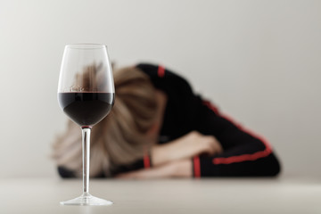 Glass with alcohol on blurred view of a lonely and desperate drunk woman lying on a table. Shallow depth of field