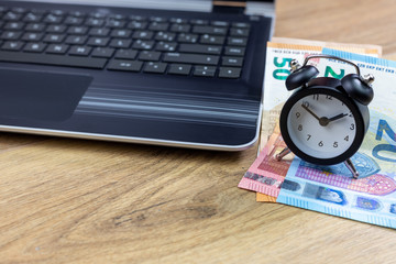 business time and money concept, laptop with money and black clock 