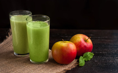 green refreshing smoothie of kiwi, Apple, avocado or banana with mint in two glasses. in front of a mint leaf and red apples. Breakfast for two