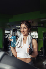 Fototapeta na wymiar Young fit woman with a towel on her shoulders holding water bottle on a treadmill. Weight Loss Concept, Aerobic Workout