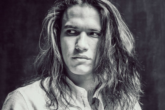 Handsome Calm Man. Portrait Of A Young Muscular Guy With Long Hair. Strong Boy On An Isolated Dark Background In The Studio